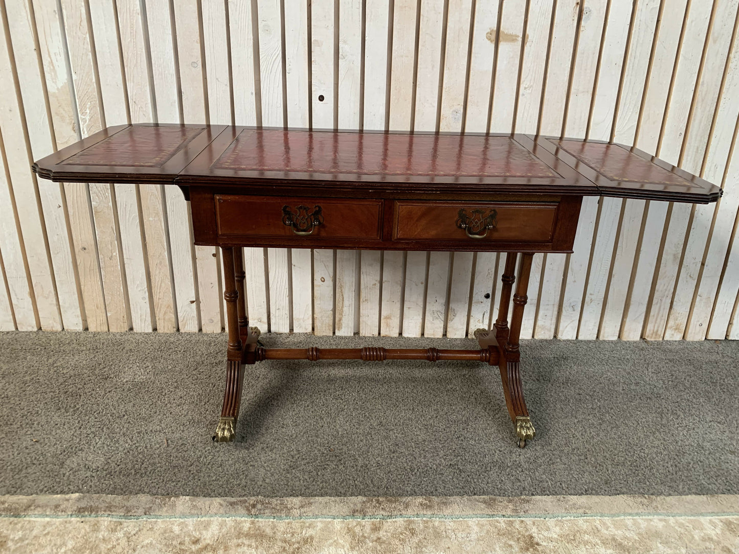 Antique drop-leaf Pembroke table with a leather top and brass claw feet.