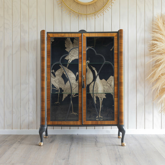 A stunning Art Deco drinks cabinet, distinguished by its unique curved top and decoupage featuring crane fabric in black and subtle gold.