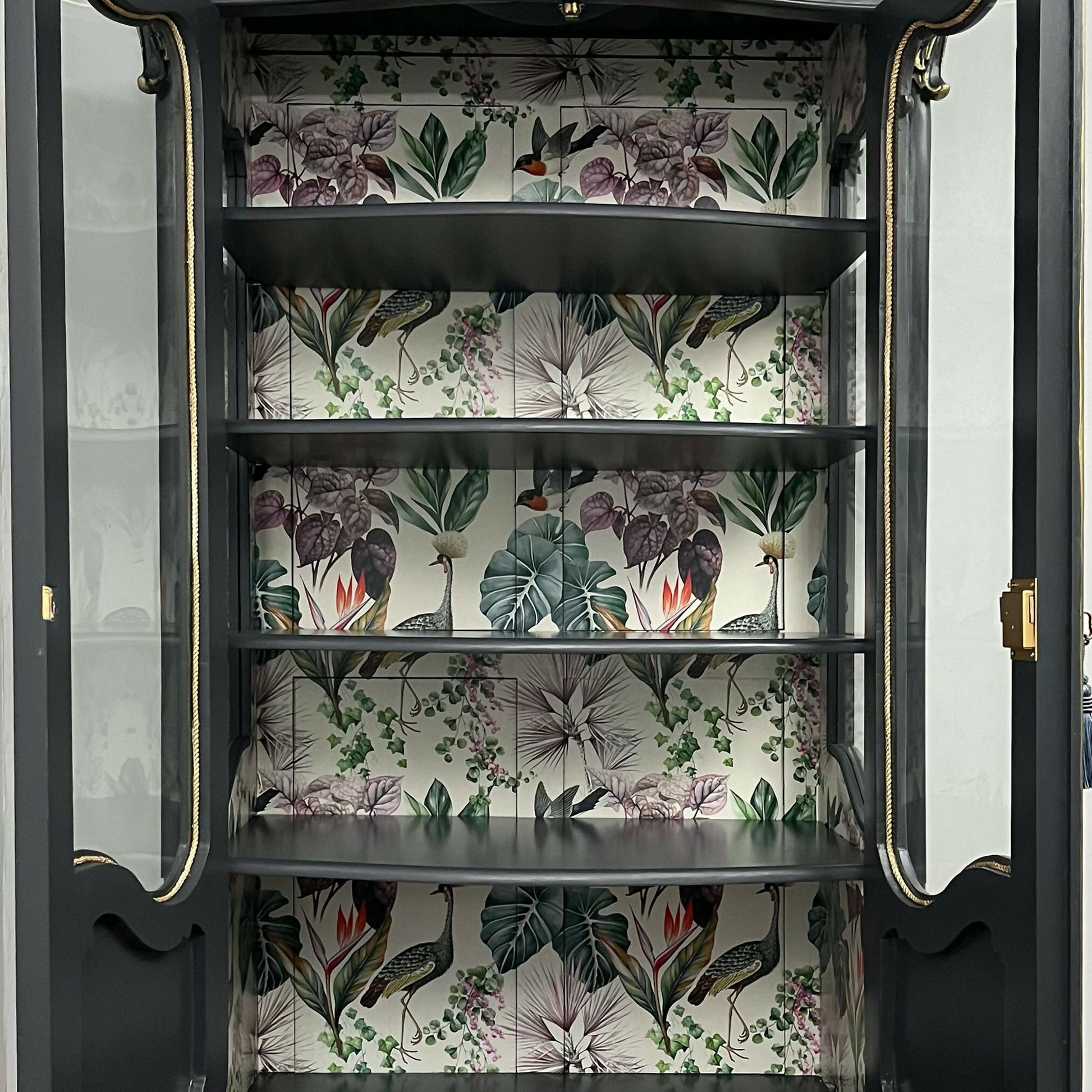 Interior shelves with botanical and bird patterned backing inside display cabinet