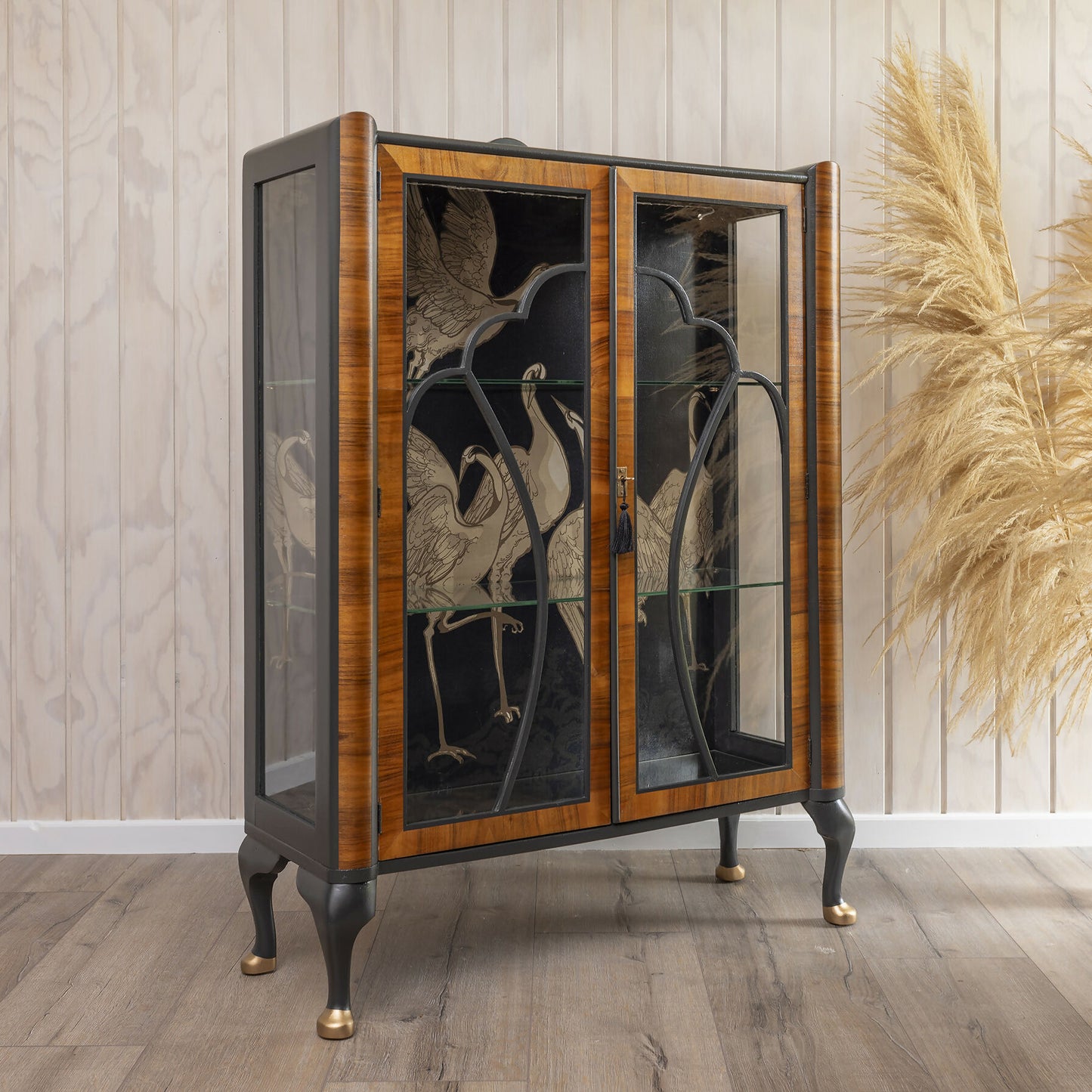 A stunning Art Deco drinks cabinet, distinguished by its unique curved top and decoupage featuring crane fabric in black and subtle gold.